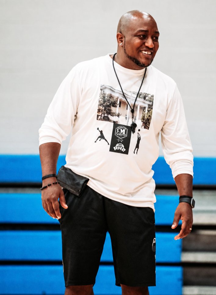 Coach Pete Marston smiling on the court, a whistle round his neck